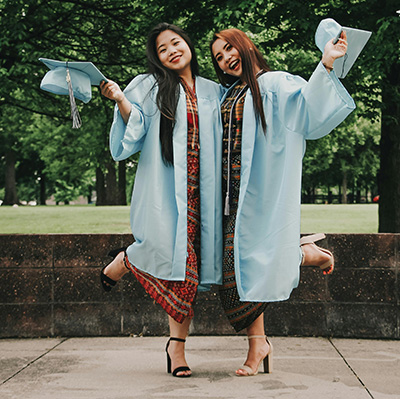 two females in graduation gowns holding their caps and posing for a picture